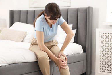 Woman suffering from knee pain on bed at home