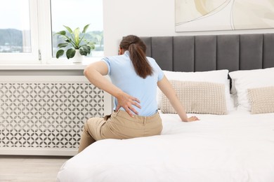 Woman suffering from back pain on bed at home, back view