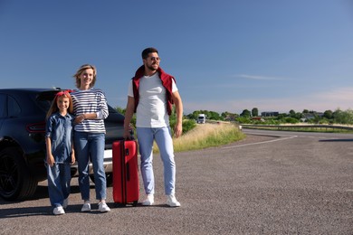 Happy family with red suitcase near car outdoors, space for text