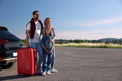 Happy family with red suitcase near car outdoors, space for text