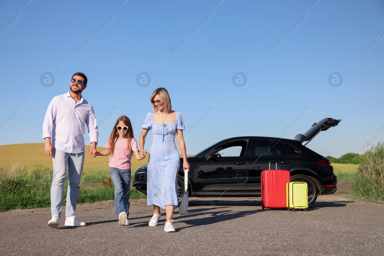 Photo of Parents, their daughter, car and suitcases outdoors. Family traveling