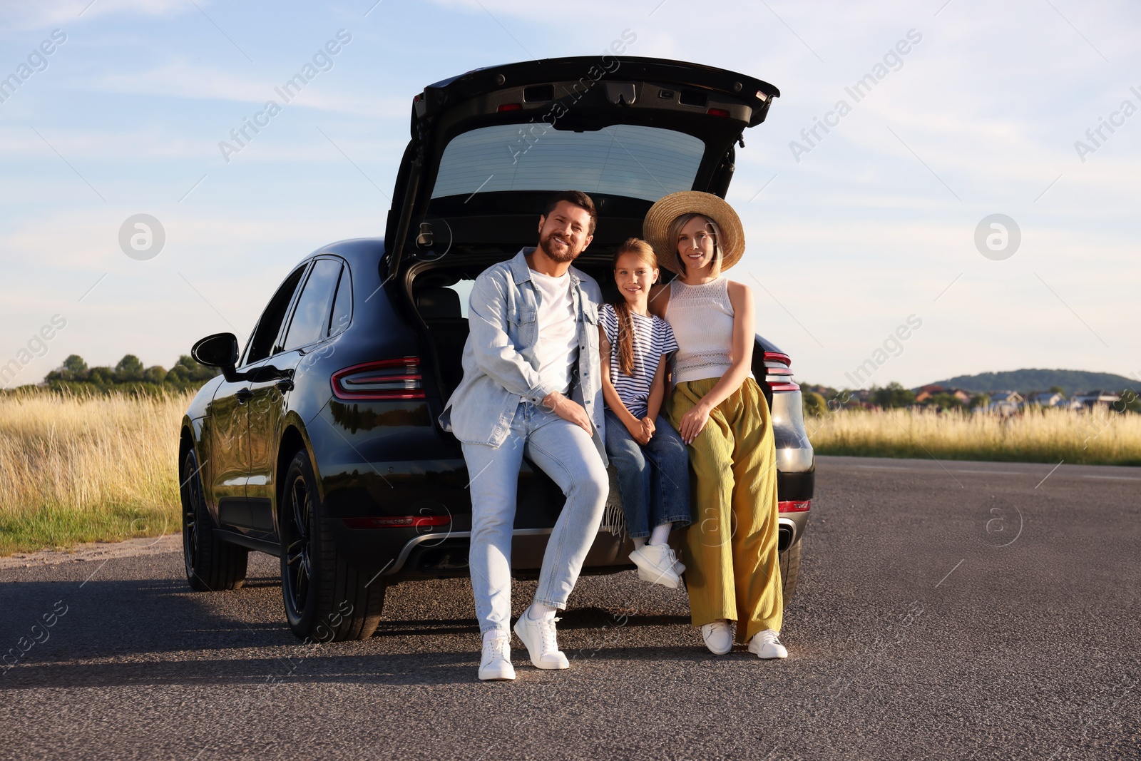 Photo of Happy family sitting in trunk of car outdoors