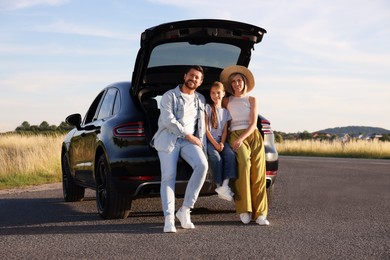 Photo of Happy family sitting in trunk of car outdoors