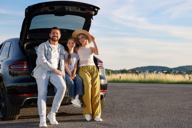 Photo of Happy family sitting in trunk of car outdoors, space for text