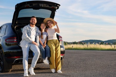 Happy family sitting in trunk of car outdoors, space for text