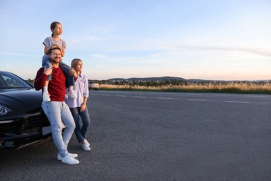 Happy parents and their daughter near car outdoors, space for text