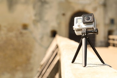 Modern action camera with tripod on wooden surface outdoors. Space for text