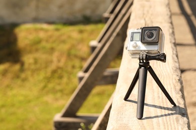 Modern action camera with tripod on wooden surface outdoors. Space for text