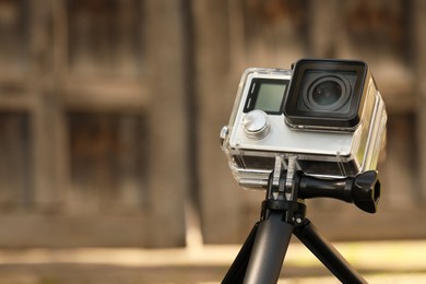 Photo of Modern action camera with tripod on blurred background, closeup. Space for text