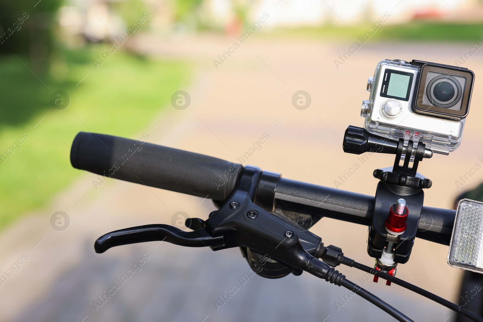 Photo of Modern action camera with mount on bicycle outdoors, closeup