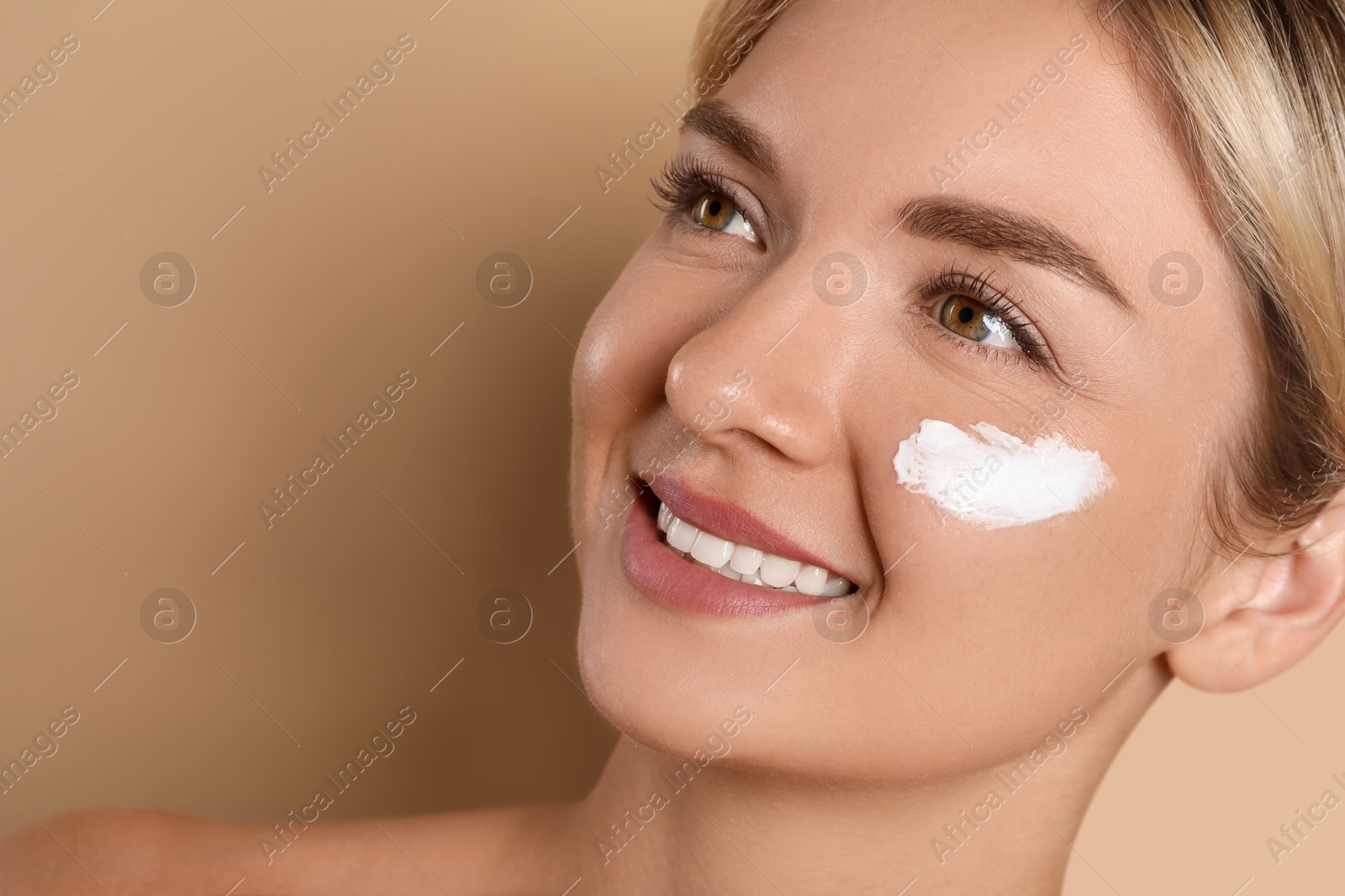 Photo of Beautiful woman with cream on her face against beige background, closeup. Space for text