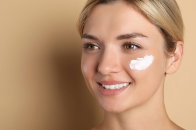 Beautiful woman with cream on her face against beige background, closeup. Space for text