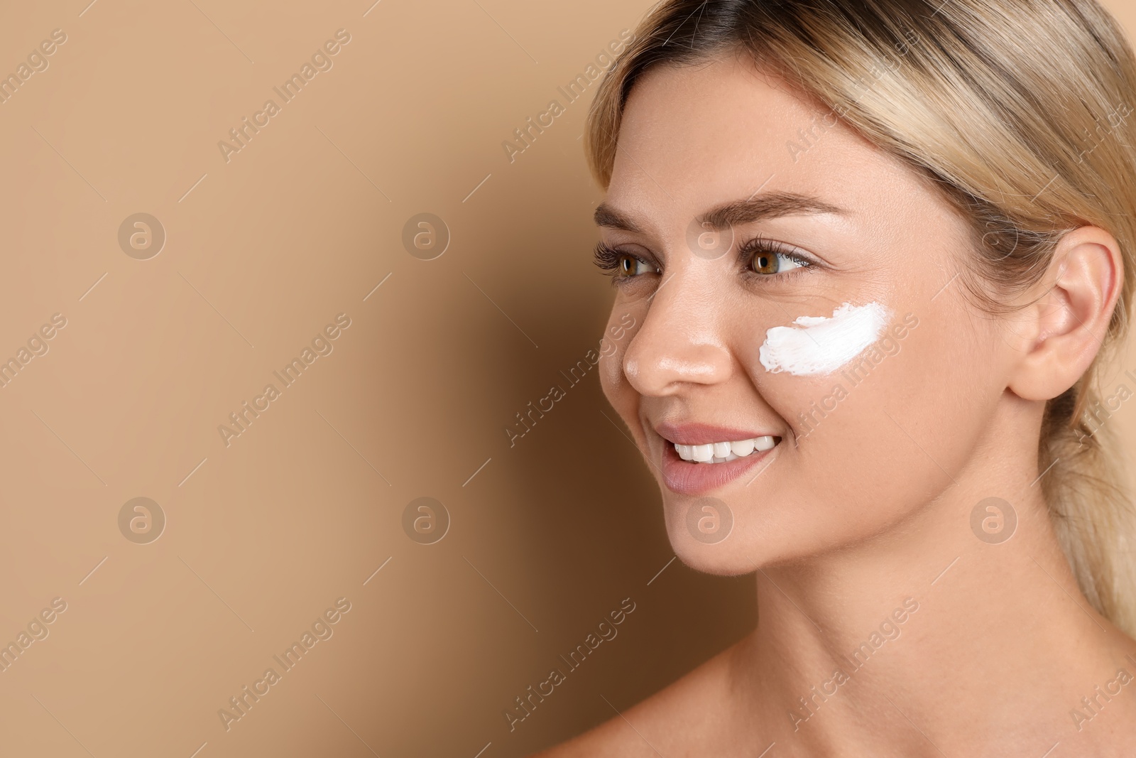 Photo of Beautiful woman with cream on her face against beige background, closeup. Space for text