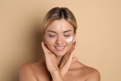 Beautiful woman with cream on her face against beige background