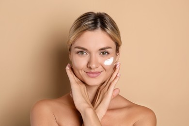 Beautiful woman with cream on her face against beige background