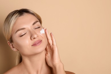 Photo of Beautiful woman with cream on her face against beige background, space for text