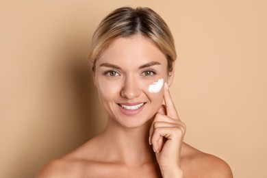 Beautiful woman applying cream on her face against beige background