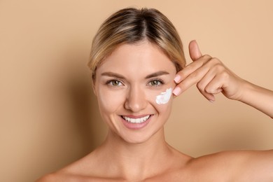 Beautiful woman applying cream on her face against beige background