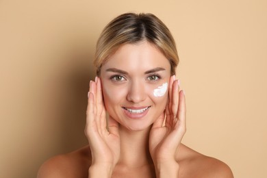 Beautiful woman with cream on her face against beige background