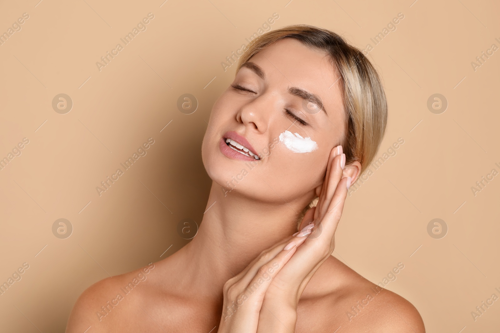 Photo of Beautiful woman with cream on her face against beige background