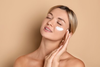 Beautiful woman with cream on her face against beige background