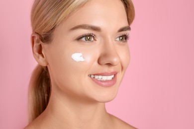 Photo of Beautiful woman with cream on her face against pink background, closeup