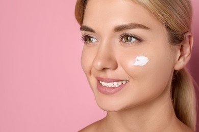 Beautiful woman with cream on her face against pink background, closeup. Space for text