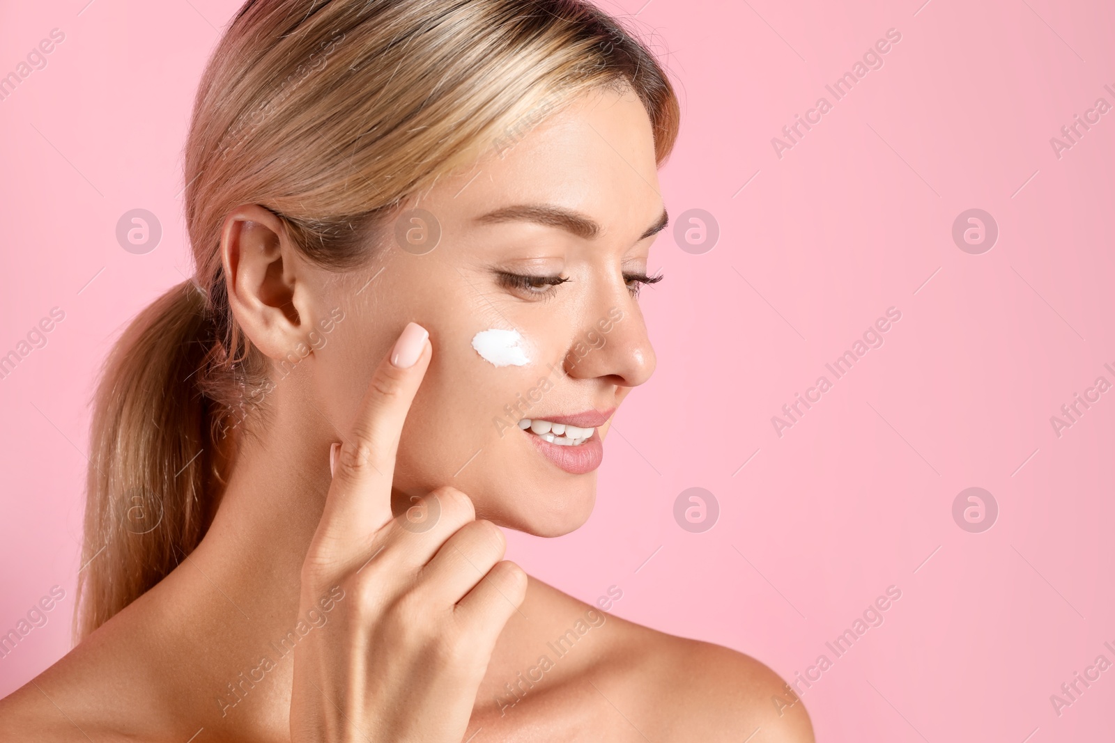 Photo of Beautiful woman applying cream on her face against pink background, space for text