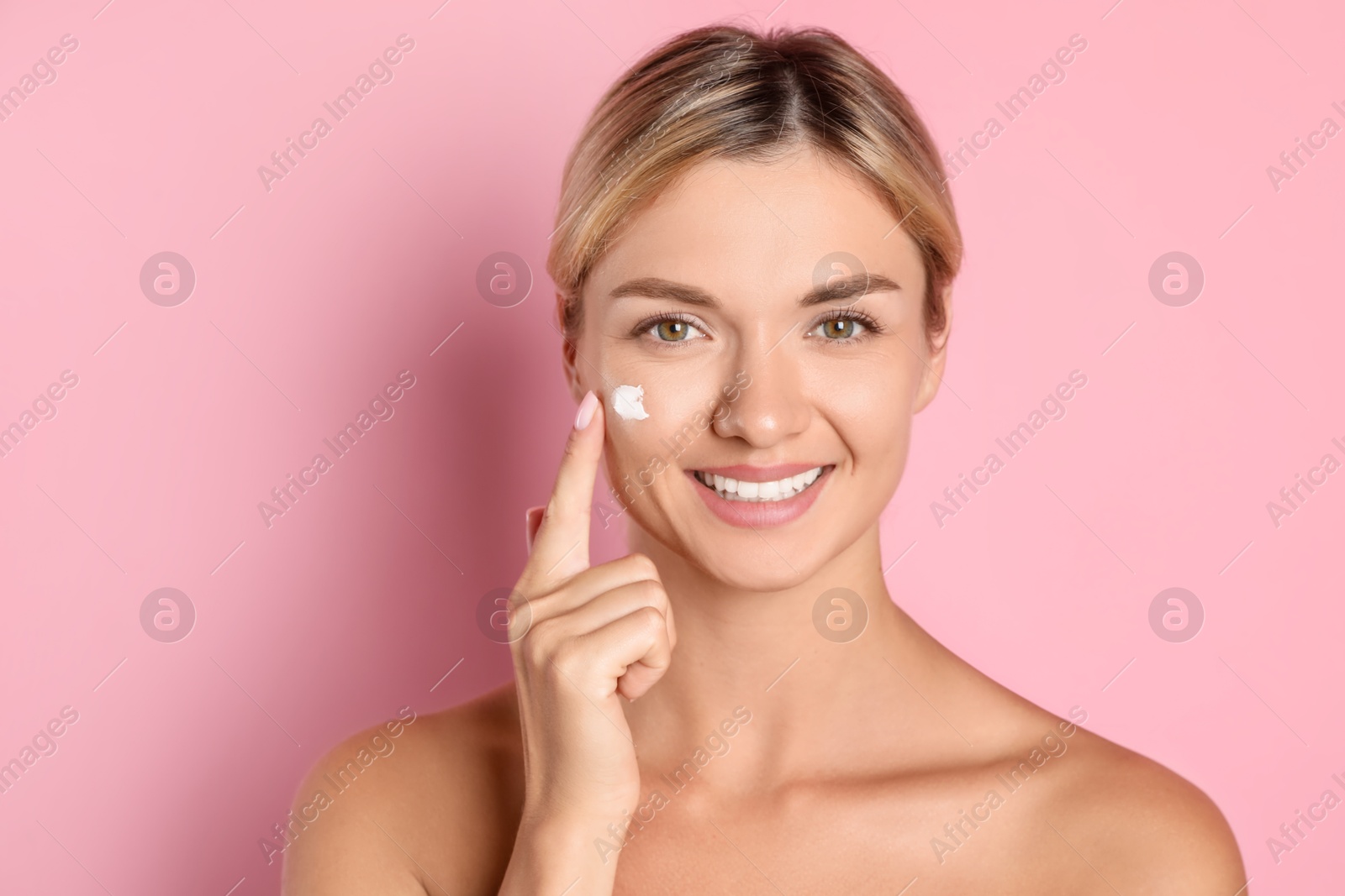 Photo of Beautiful woman applying cream on her face against pink background