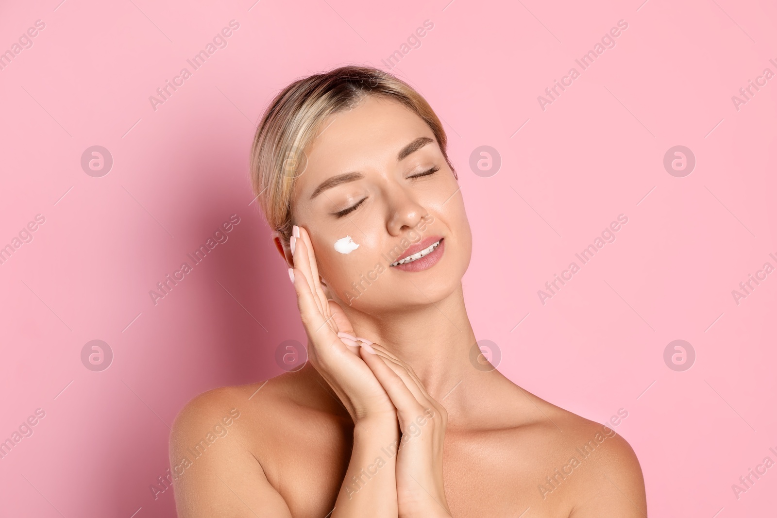 Photo of Beautiful woman with cream on her face against pink background