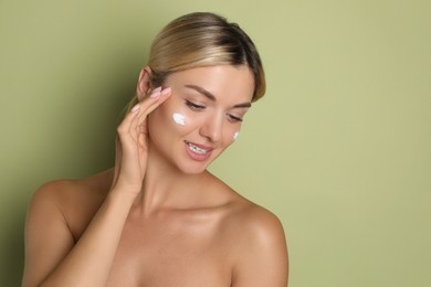 Beautiful woman with cream on her face against green background