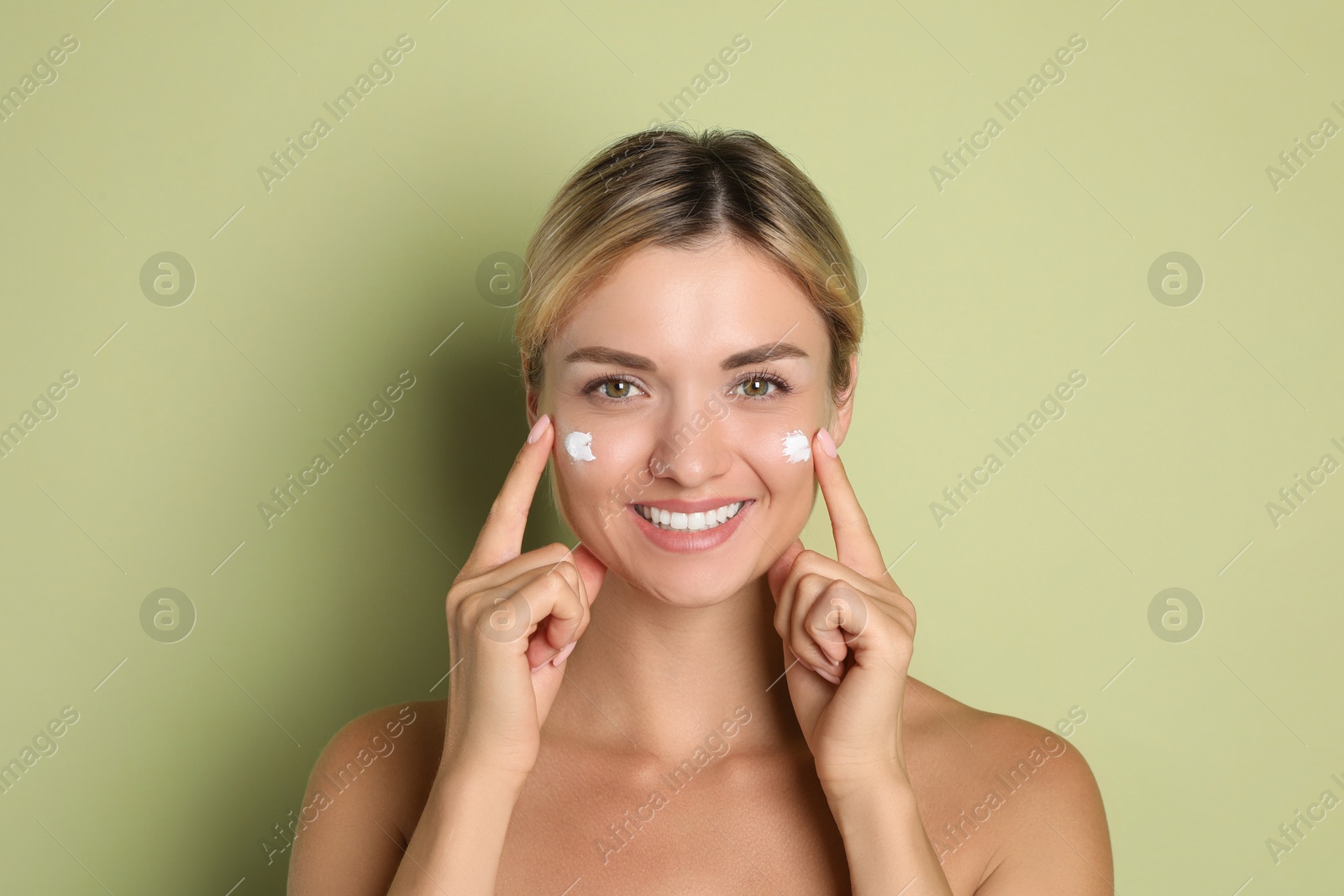 Photo of Beautiful woman applying cream on her face against green background