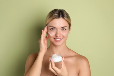 Beautiful woman with jar of facial cream against green background