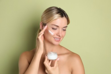 Beautiful woman with jar of facial cream against green background