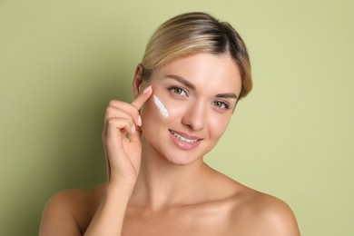 Photo of Beautiful woman applying cream on her face against green background