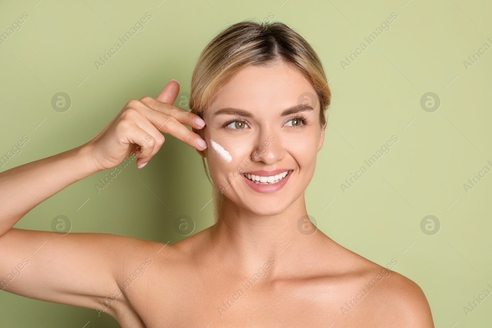 Photo of Beautiful woman applying cream on her face against green background