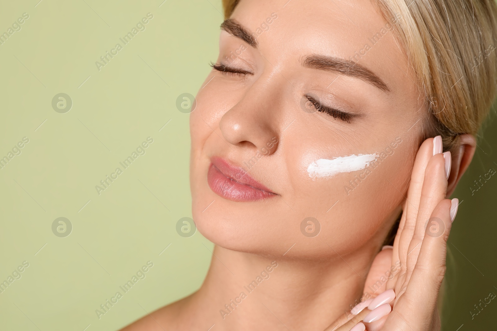 Photo of Beautiful woman with cream on her face against green background, closeup