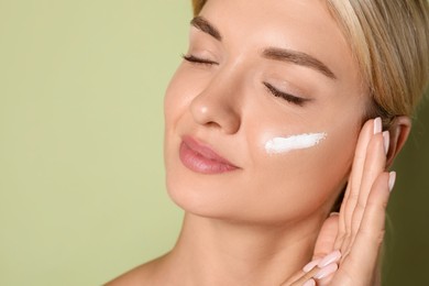 Beautiful woman with cream on her face against green background, closeup