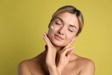 Beautiful woman with cream on her face against olive background