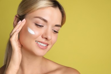 Photo of Beautiful woman with cream on her face against olive background, closeup. Space for text