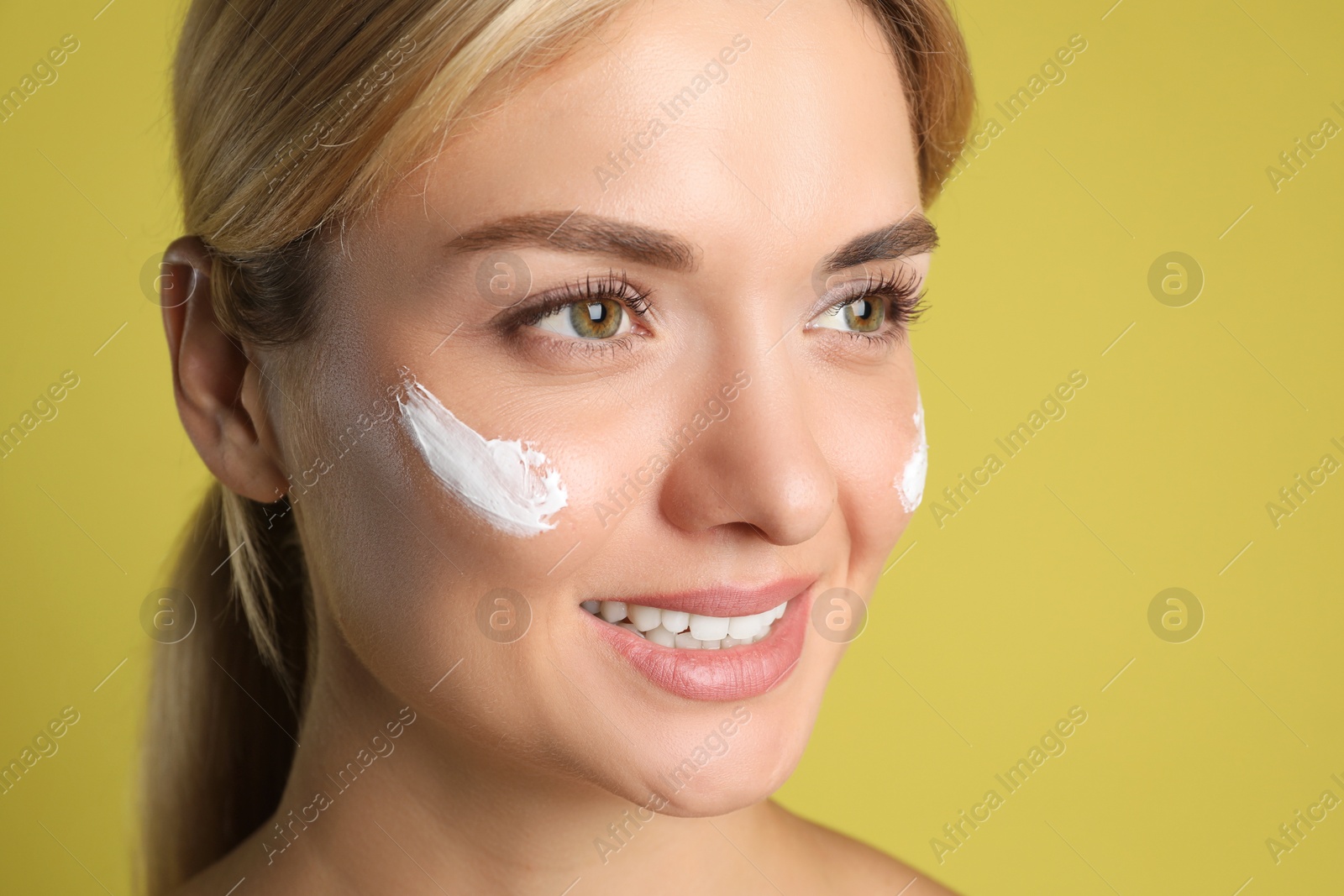 Photo of Beautiful woman with cream on her face against olive background, closeup