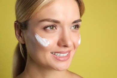 Beautiful woman with cream on her face against olive background, closeup