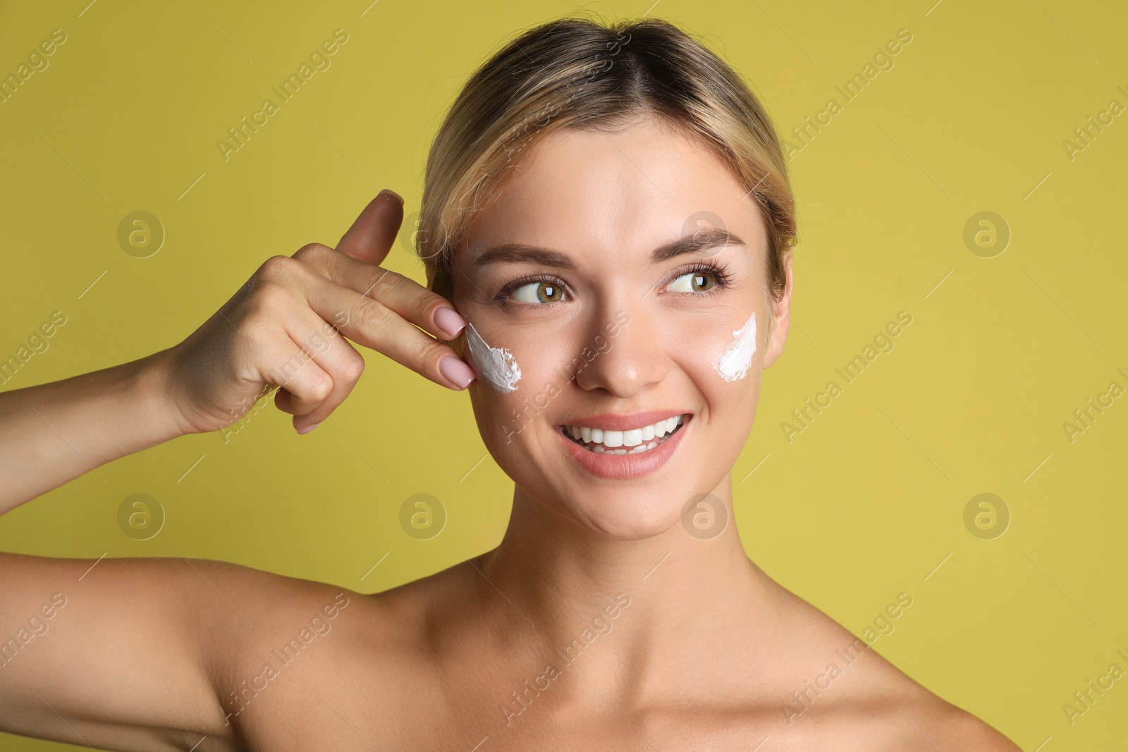 Photo of Beautiful woman applying cream on her face against olive background