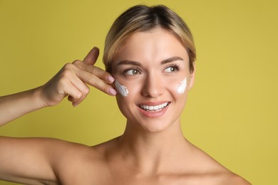 Beautiful woman applying cream on her face against olive background