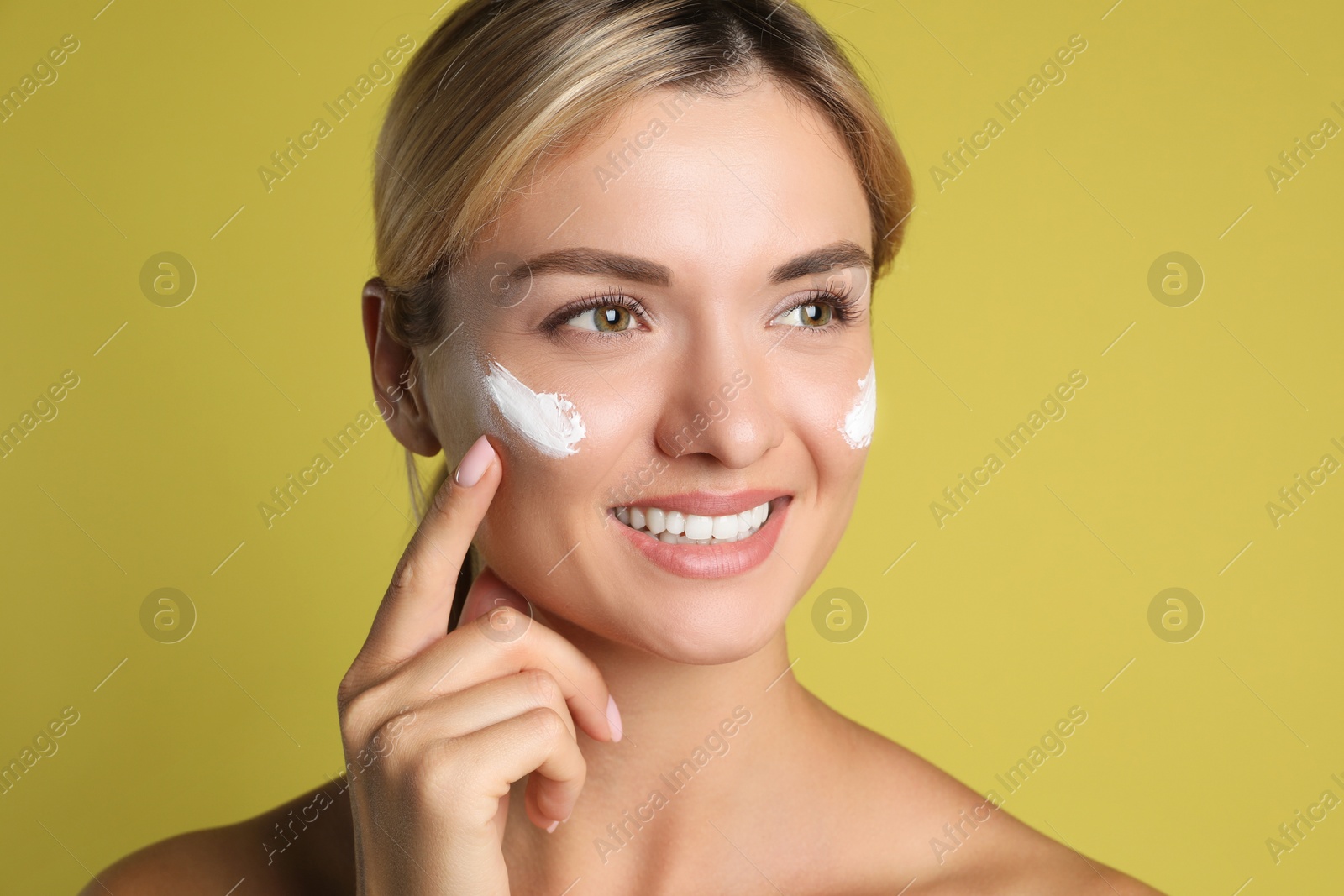 Photo of Beautiful woman applying cream on her face against olive background