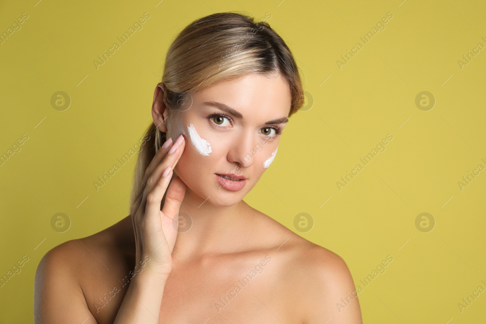 Photo of Beautiful woman applying cream on her face against olive background, space for text