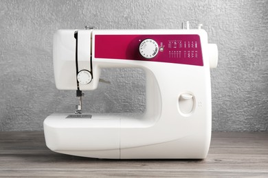 Photo of White sewing machine on wooden table against gray wall