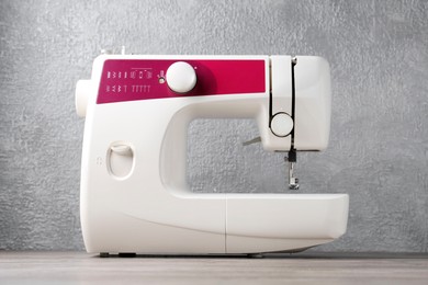 White sewing machine on wooden table against gray wall