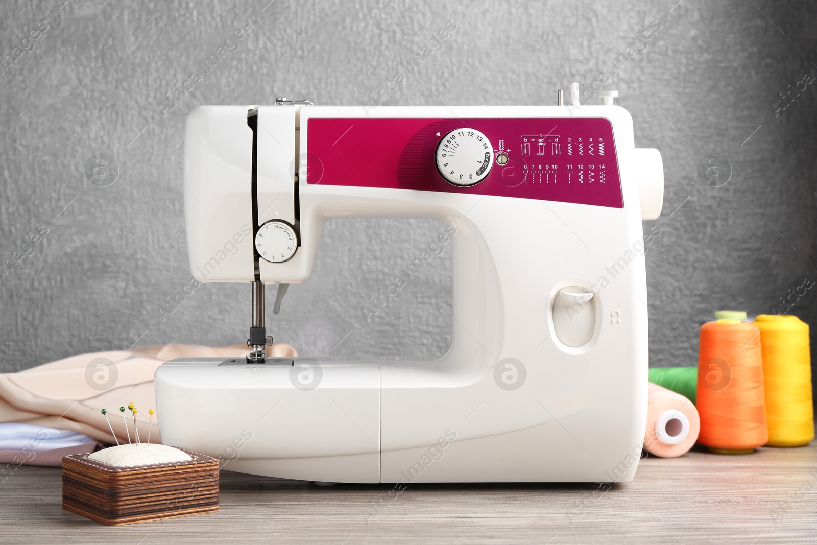 Photo of White sewing machine and craft accessories on wooden table against gray wall