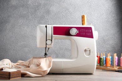 Photo of White sewing machine with beige fabric and craft accessories on wooden table near gray wall